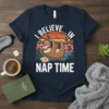 T-shirt with "I Believe In Nap Time" text and a cute sloth hanging from a branch, with a sunset graphic