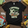 I CRUSHED 100 DAYS ELEMENTARY LEVEL COMPLETE text with a monster truck graphic and colored pencils on a black t-shirt