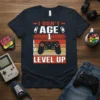 I DON'T AGE 1 LEVEL UP text with video game controller and progress bar graphic on a navy t-shirt
