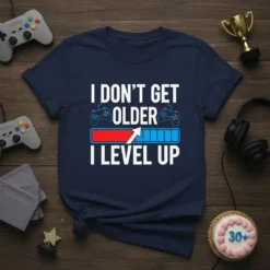I DON'T GET OLDER I LEVEL UP text with a gaming progress bar and controllers graphic on a navy t-shirt