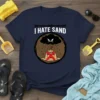 Navy blue t-shirt with "I HATE SAND" text and a graphic of an angry cloud raining on a sandcastle with