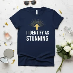 Navy blue t-shirt with white text "I IDENTIFY AS STUNNING" and gold glitter arrow graphic above