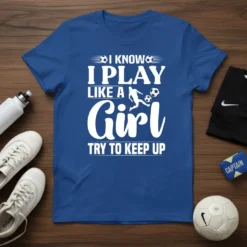 White text quote "I Know I Play Like A Girl Try To Keep Up" on a blue t-shirt, featuring soccer