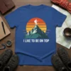 I Like To Be On Top mountain climber t-shirt design with a silhouette on a peak against a sunset graphic