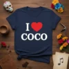 Navy blue t-shirt with white text "I" and "COCO" sandwiching a red heart graphic, featuring the phrase "I Love Coco"