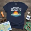 I Love Downtown Sarasota text with a stylized skyline, bridge, palm trees, and sunset graphic on a navy blue t-shirt