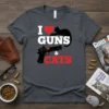 I LOVE GUNS & CATS t-shirt design featuring white text, a red heart, a black cat, a black handgun, and