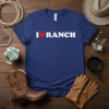 I Love Ranch text with a red heart graphic on a navy blue t-shirt, featuring western-themed props like a cowboy