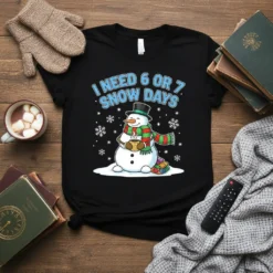 T-shirt with "I NEED 6 OR 7 SNOW DAYS" text and a cute snowman holding a mug