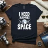 Navy t-shirt with white text "I NEED MORE SPACE" featuring a graphic of the moon and clouds, designed for astronomy