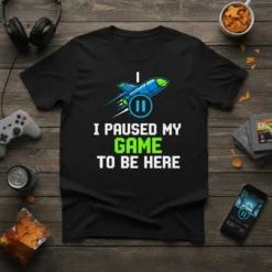 Black t-shirt with white text "I PAUSED MY GAME TO BE HERE" and a blue rocket graphic with a pause
