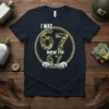 T-shirt with "I WAS 67 NOW I'M 67" text in camouflage font, featuring hands holding the number 67