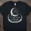 Black t-shirt with white text "I'm Flying Trough A Phase" and a black cat riding a broomstick across a crescent