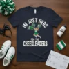 Navy blue t-shirt with white text "I'm Just Here For The Cheerleaders" and a cartoon cheerleader graphic holding pom-poms