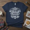 White text design "I'm My Mother-in-Law's Favorite Child" on a navy blue t-shirt, featuring decorative elements and hearts