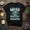 I'm Not Just A Mess I'm A Beautifully Organized Disaster quote on a black t-shirt with teal and white typography