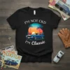 Black t-shirt with white text "I'm Not Old I'm Classic" above a blue vintage car graphic with palm trees and