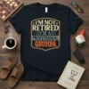 I'm Not Retired I'm A Professional Grumpa text design on a black t-shirt, featuring vintage-style typography and a shield emblem