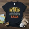 I'm Not Retired I'm A Professional Lala quote on a navy blue t-shirt, featuring distressed yellow and orange text