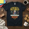 T-shirt with "I'm Not Retired I'm A Professional Nonny" text and a cartoon graphic of a grandmother surrounded by toys