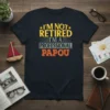 T-shirt with yellow and orange text that reads "I'm Not Retired I'm A Professional Papou" on a navy background