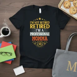 Black t-shirt with "I'm Not Retired Retired I'm A Professional Momma" text in yellow, white, and orange. Features star graphics