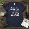Navy blue t-shirt with white text that reads "I'm not a witch WITCH I'm your WIFE!", featuring a purple witch