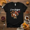 Black t-shirt with white text "I'm Stuffed" and a cartoon turkey holding baby feet graphic, autumn leaves