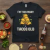 Black t-shirt with "I'm This Many Tacos Old" text and a pile of tacos graphic, celebrating age with humor