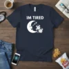 T-shirt with "IM TIRED" text, a sleeping moon graphic, and alarm clocks with Zzz symbols