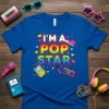 I'm A Pop Star text in rainbow gradient with retro 80s graphics like boombox and microphone on a blue t-shirt