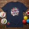 Vibrant "i'm the Birthday Girl!" text with colorful cakes, candles, and confetti graphic on a navy t-shirt