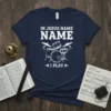 Navy blue t-shirt with white text "IN JESUS NAME NAME I PLAY" and a drum set graphic. Includes Bible and