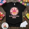 In My Birthday ERA text with a cute cupcake graphic, balloons, gifts, and party hats on a black t-shirt