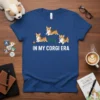 Blue t-shirt with white text "In My Corgi Era" and three cartoon corgis playing with a ball and jump obstacle