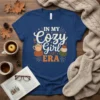In My Cozy Girl ERA text with coffee cup and pumpkins graphic on a blue t-shirt