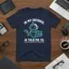Navy t-shirt with "In My Defense AI Told Me To" text and a cartoon robot holding a tablet displaying binary