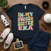 Retro graphic t-shirt with colorful text "IN MY SOCCER SISTER ERA" and a soccer ball with a bow