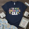 Retro "In My Surrogate Era" text design with colorful lettering, hearts, and smiley faces on a navy blue t-shirt