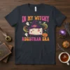 In My Witchy Registrar Era text with witch hat, open book, ghosts, and pumpkin graphic on a dark t-shirt