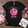 In October We Wear Pink t-shirt design with a witch flying on a broomstick, a pink ribbon, moon, and castle