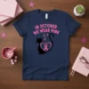 Navy t-shirt with pink text "In October We Wear Pink" and a black cat silhouette holding a pink ribbon heart