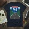 Interstate 94 highway sign graphic on a navy blue t-shirt, depicting a winding road and city skyline