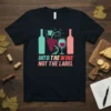 Into The Wine Not The Label quote on a black t-shirt with wine bottle, grape, and wine glass graphic