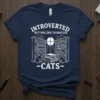 T-shirt with "Introverted But Willing to Discuss Cats" text, featuring bookshelves and cats, white outline design on navy shirt