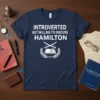 Navy t-shirt with white text "INTROVERTED BUT WILLING TO DISCUSS HAMILTON" and a laurel wreath with crossed swords and a