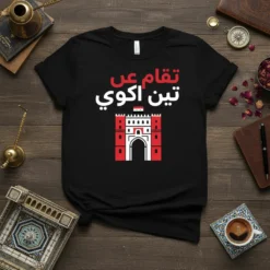 Black t-shirt with Arabic text "تقام عن تين اكو" and a red and white graphic of a historic Iraqi landmark