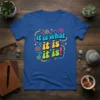 Blue t-shirt with "it is what it is it is it is!" in colorful retro font and swirling graphics