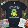 Dark t-shirt with "IT'S GOOD TO SEE I'M NOT THE ONLY UGLY PERSON HERE" text and a green monster graphic