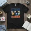 Black t-shirt with retro design: "IT'S ME HI I'M THE PROBLEM" in colorful block letters, featuring a lightbulb, question mark